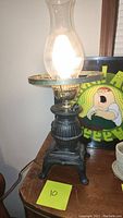 Front view of the lamp showing the lit bulb and clear glass hurricane shade with ornate cast iron base.