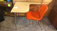 Front and side view of vintage school desk with orange plastic chair, showing wooden desk top, chrome metal frame, and attached chair.