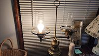 Full view of the two-sided brass lamp with two lit bulbs under glass chimneys.