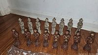 Photo showing two complete groups of chess pieces in contrasting white and reddish-brown colors on wood floor.