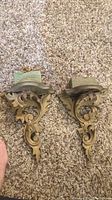 Pair of ornate decorative wall shelves with antique finish and green foam padding on platforms laid on carpeted floor.