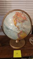 Front view of the globe showing North and South America clearly. Globe mounted on brass base with metal meridian support at the sides.