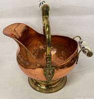 Front angle view showing copper body, brass base and pouring spout, with ceramic-handled brass handle over the top.