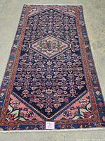 Full view of the entire rug laid flat on a concrete floor, showing shape, borders and end fringe.