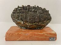 Front view of metal cityscape relief sculpture of Jerusalem mounted on stone base.