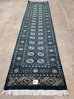 Full-length view of green Bokhara design wool runner with ivory fringe