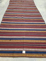 Full view of the hand knotted Kelim carpet showing the full length and pattern of multicolored horizontal stripes on concrete floor.