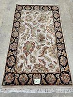 Full view of the hand knotted Sarough design carpet showing overall floral pattern, cream center field and black border with floral motifs and fringed edges.