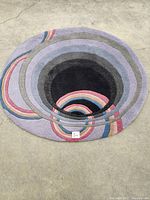 Full view of the round rug showing concentric color bands and overall shape on concrete floor.