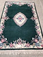 Full top view of the green hand tufted Savonnerie carpet with floral motifs and fringed edges.