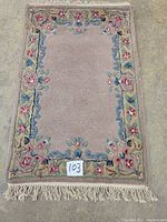 Full view of hand tufted Savonnerie wool rug showing overall floral border and central field with fringed ends.