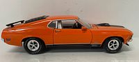 Side view of the orange 1970 Ford Mustang Mach 1 model showing black racing stripes and rear spoiler