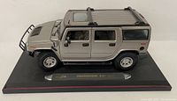 Side angle showing silver Maisto Hummer H2 SUV model mounted on display base with detailed body and tires.