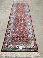 Full view of red runner with cream borders and fringed ends laid flat on concrete floor