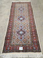 Full view of the entire runner laid flat on concrete floor showing overall shape, pattern, borders and fringe