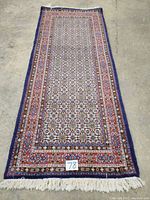 Full view of Persian hand knotted carpet laid flat, showing whole rug and fringed ends, with lot number card placed near one end.
