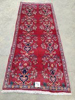 Full view of rectangular red wool rug with floral patterns and cream fringes laid flat on concrete floor