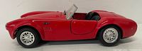 Side view of the red Shelby Cobra car model showing chrome wheels and interior