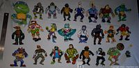 Photo of approximately 25 vintage TMNT figures including turtles, villains, and allies on a white background with ruler for scale.