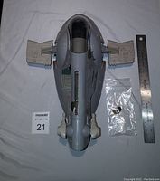 Top view of gray vintage Slave 1 ship body with attached side wings and small bag of additional parts alongside metal ruler for scale.