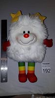 Front view of 12 inch white fluffy Twink plush with yellow star antennae, red gloves, and rainbow striped legs alongside a ruler for size comparison.