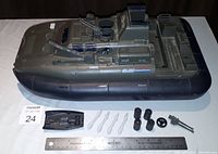 Top-down view of the G.I. Joe Killer Whale hovercraft with loose parts arranged in front, including small black skiff, clear propeller blades, wheels, and steering wheel next to a ruler.