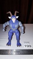 Front view of Mongor action figure standing upright with arms posed. Ruler included for size reference, showing figure approximately 6 inches tall.
