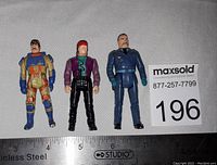 Front view of three M.A.S.K action figures lined up on a cloth background with measuring scale at bottom and lot number on right.