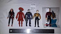 Five Star Trek Playmates action figures displayed on a gray surface with a measuring ruler below them for scale. The fifth figure holds a shield, a chair, and a red rod accessory.