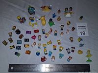 Photo showing an assortment of small Squinkies figurines including Disney characters such as Mickey Mouse, Minnie, Beauty and the Beast, Dumbo, Ariel, Tinker Bell, and others scattered on a surface.