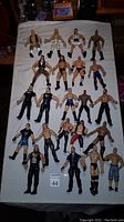 Top view of 22 wrestling action figures arranged in four rows on a white cloth. Figures vary in clothing color and style, many showing signs of wear consistent with used figures from the 1990s.