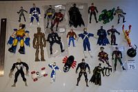 Top-down photo of 24 Marvel and DC superhero action figures arranged with a ruler for scale, including iconic characters such as Wolverine, Batman, and Iron Man in used condition.