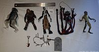 Top down view of six McFarlane action figures including ghostly figure, monster, tattered coat character, multi-limbed red creature, amphibious figure, and accessories like shovel and tombstone plaque. A ruler for scale is included.