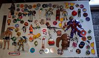 Top-down photo showing a variety of pogs, toy cars, action figures, and stickers arranged on a white surface