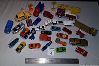 Top view of a variety of toy cars and trucks arranged on a white cloth, including a large yellow fire truck and assorted miniature vehicles and traffic signs.