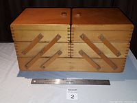 Front view of the closed vintage wooden storage box with leather straps and dovetail joints visible, ruler for size reference.