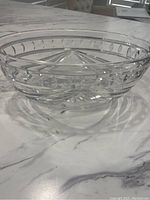 Clear crystal glass bowl placed on marble surface showing detailed cut pattern on side.