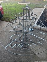 Front and side view of large silver metal chandelier frame on pavement outdoors.