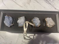 Set of four blue and gold napkin rings featuring raw crystal clusters mounted on black foam inside a box.
