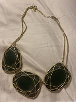 Full view of necklace laid flat showing three large green stones with gold wire overlay attached to gold chain.