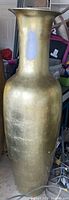 Full length image of large gold-toned floor vase showing shape, texture, and paint mark on neck.
