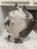 Front view of the large pottery cat sculpture with black and white shading and incised facial details.