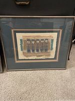 Framed mixed media artwork with vertical geometric shapes in blue and brown tones lying on carpet