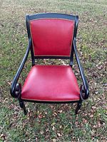Front view of red leather chair with black wooden frame and brass nailhead trim showing curved arms and seat.