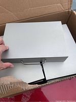 Photo of five silver-colored rectangular jewelry cases stacked inside a cardboard box showing metal handle on the front.