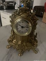 Front view of ornate brass Urania quartz clock with Roman numeral dial, showing detailed decorative design.