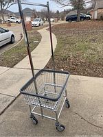 Front-side view of metal washroom cart showing wire basket with rubber trim, tall handle, and caster wheels.
