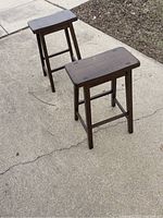 Two wooden stools on concrete ground showing shape, design and surface condition.