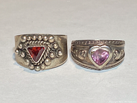 Front view of two sterling silver rings. The left ring has a red triangular crystal with silver bead embellishments. The right ring has a pink heart-shaped crystal with decorative hearts on the band.
