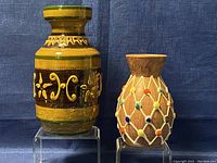 Two vintage handmade pottery vases displayed side by side on stands against a blue background.
